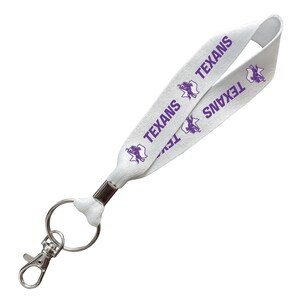 May include: A white fabric lanyard featuring a repeating purple graphic of a bull and the text TEXANS. The lanyard includes a silver-toned metal crimp, a circular split ring, and a spring-loaded lobster claw clasp for attaching keys or identification.