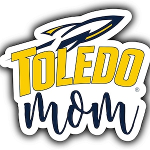 May include: A die-cut sticker featuring the words "TOLEDO Mom" in yellow and navy blue. The word "TOLEDO" is in bold, block letters, with a rocket ship graphic above it. The word "Mom" is in a cursive font.