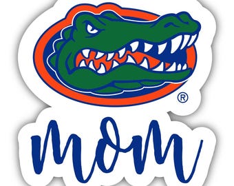 May include: A white sticker with a green alligator head in an orange circle with a blue outline. The text "mom" is written in blue cursive below the alligator.