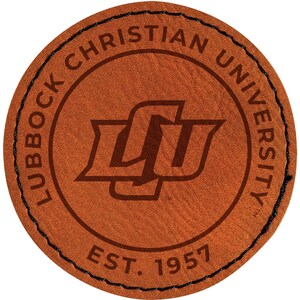 May include: A round, brown leather patch with the text "Lubbock Christian University" encircling the edge. The university logo is in the center, with "EST. 1957" below. The patch has a stitched black border.