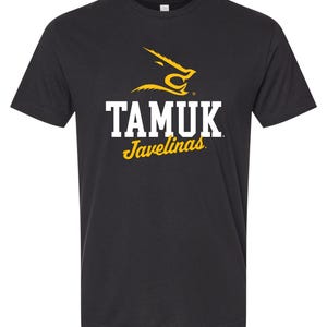 May include: A black short-sleeve t-shirt featuring a yellow graphic of a javelina head above the white text TAMUK and the yellow script text Javelinas centered on the chest. The design includes a small registered trademark symbol near the logo.