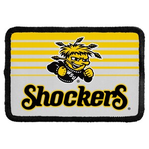 May include: A rectangular patch with a black stitched border featuring a yellow and white horizontal striped background. In the center is a yellow cartoon character with wheat stalks on its head and the text Shockers in large black script.