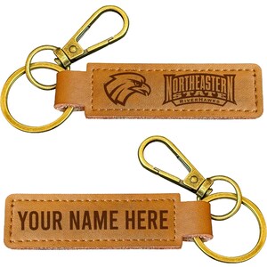 May include: Two rectangular tan keychains with antique brass hardware, including a lobster clasp and a split ring. One keychain features the Northeastern State Riverhawks logo and text, while the other displays the placeholder text YOUR NAME HERE.