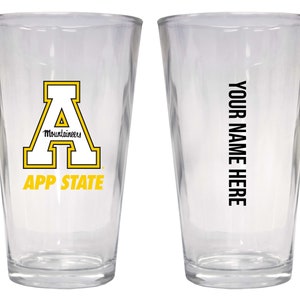 May include: Two clear glass pint glasses. One glass features a white "A" with a yellow outline and the text "App State Mountaineers". The other glass has the text "Your Name Here" in black.