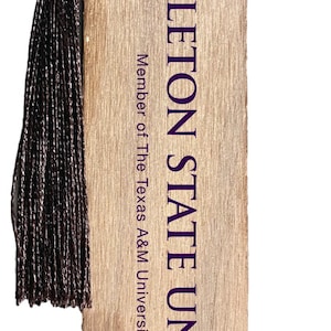 May include: Wooden bookmark featuring the Tarleton State University logo and text in purple. The bookmark has a brown tassel attached to the top. The text "Member of The Texas A&M University System" is also printed on the bookmark.