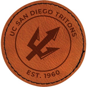 May include: A round, brown leather patch with the text "UC San Diego Tritons" around the top and "EST. 1960" at the bottom. A trident logo is in the center. The patch has a black stitched border.