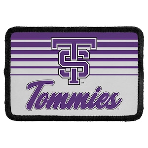May include: A rectangular patch with a black stitched border featuring a purple and white striped background. The design includes a large purple and white TS monogram logo above the purple script text Tommies with a trademark symbol.