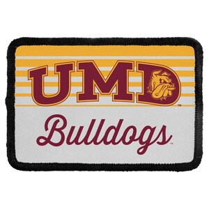 May include: A rectangular patch with a black stitched border. The top section features yellow and white horizontal stripes with the maroon text UMD and a bulldog mascot logo. The bottom section is white with the maroon script text Bulldogs.