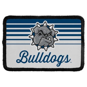 May include: A rectangular fabric patch with a black stitched border. The design features horizontal navy blue and white stripes, a central graphic of a grey bulldog wearing a spiked collar, and the word Bulldogs written in navy blue script.