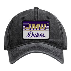 May include: A charcoal grey baseball cap with a distressed finish featuring a rectangular patch on the front. The patch displays the purple and gold text JMU above the word Dukes in purple script, set against a background of horizontal stripes.