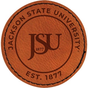 May include: A round, brown leather patch with the text "JACKSON STATE UNIVERSITY" around the outer edge. The center features the letters "JSU" and the year "1877". The patch is stitched with black thread.