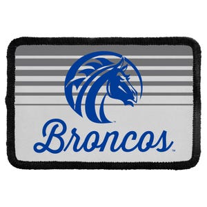 May include: A rectangular patch with a black stitched border featuring a grey and white horizontal striped background. A blue horse head logo is centered above the blue script text that reads Broncos, with a small trademark symbol included.