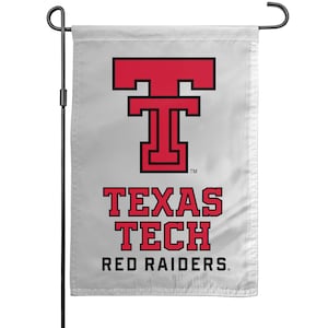 May include: A white garden flag featuring the Texas Tech Red Raiders logo. The logo is a red "T" with a black outline, above the words "TEXAS TECH RED RAIDERS" in red block letters. The flag is mounted on a black metal pole.
