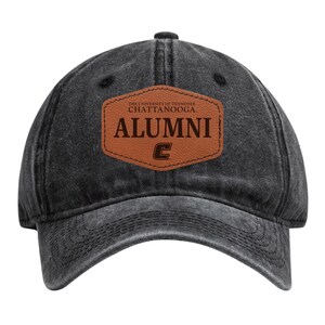 May include: A black, distressed-look baseball cap with a curved brim. A brown leather patch on the front displays the text "ALUMNI" and "THE UNIVERSITY OF TENNESSEE CHATTANOOGA" in white and brown lettering, along with a "C" logo.