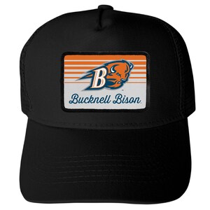 May include: A black trucker hat featuring a rectangular patch on the front. The patch displays an orange and blue bison head logo, the letter B, and the text Bucknell Bison in blue script against a background of horizontal orange and white stripes.