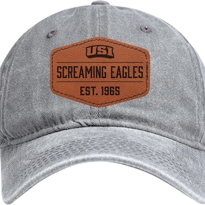 May include: Gray baseball cap with a curved brim and a brown leather patch. The patch features the text "USI SCREAMING EAGLES EST. 1965" in a bold, vintage font. The cap has a pre-worn, faded appearance.