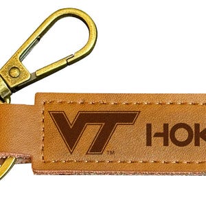 May include: A brown leather keychain with a gold metal key ring and a clip. The keychain has the text "VT Hokies" in brown lettering.