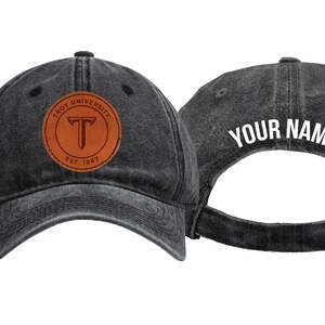 May include: Two charcoal gray baseball caps. One cap features a brown leather patch with "TROY UNIVERSITY" and "EST. 1887". The other cap has "YOUR NAME" in white lettering on the back. Adjustable metal buckle closure.