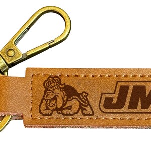 May include: A brown leather keychain with a gold metal key ring and a snap hook. The keychain has a brown leather tag with the text "JMU" and a graphic of a bulldog wearing a crown.