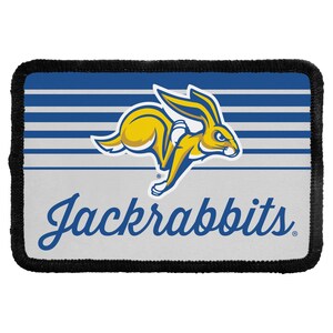 May include: A rectangular patch with a black stitched border featuring a blue and white horizontal striped upper section and a light gray lower section. A yellow and blue leaping jackrabbit graphic is centered above the blue text Jackrabbits.