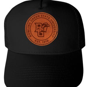 May include: Black trucker hat featuring a brown leather patch with the Bowling Green State University logo and the text "EST. 1910". The hat has a curved brim and a mesh back.