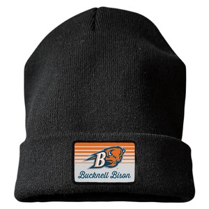 May include: A black knit beanie featuring a rectangular patch on the front. The patch displays an orange and white striped background with a blue letter B, a bison head graphic, and the text Bucknell Bison in a blue script font.