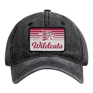 May include: A charcoal grey baseball cap with a distressed finish. Centered on the front is a rectangular patch featuring a maroon and white striped background, a stylized grey and maroon wildcat head graphic, and the word Wildcats in maroon.