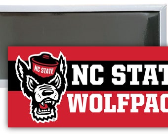 May include: A red and black magnet featuring the NC State Wolfpack logo. The logo depicts a wolf wearing a red and black hat with the words "NC State" on it. The words "NC State" and "Wolfpack" are in white lettering on a black background.