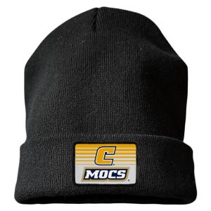 May include: A solid black knit beanie featuring a rectangular patch on the front cuff. The patch displays a large yellow letter C above the word MOCS in dark blue capital letters, set against a background of horizontal white and yellow lines.