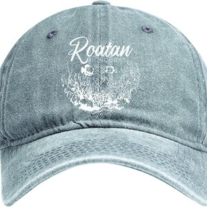 May include: A faded denim baseball cap with the word "Roatan" in white script. Below the text is a white graphic of coral and sea life. The cap has a curved brim and a button on top.