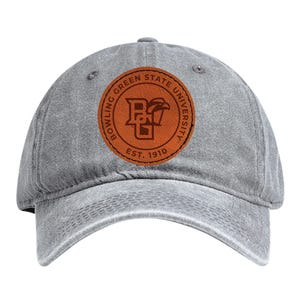 May include: A gray baseball cap with a curved brim. The cap features a circular brown leather patch with the words "Bowling Green State University" and "Est. 1910" encircling a logo.