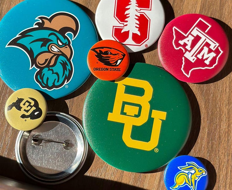 a collection of colorful pin badges, each featuring different logos and designs, including a blue pin with a bird logo, a green pin with a yellow "B" logo, and a red pin with the letters "ATM" and a map of the United States.