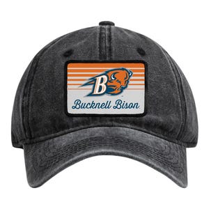 May include: A charcoal grey baseball cap with a distressed finish featuring a rectangular patch on the front. The patch displays an orange and white striped background with a blue bison head logo, a large letter B, and the text Bucknell Bison.
