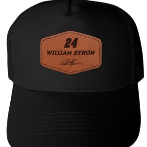 May include: Black trucker hat with a mesh back and a curved brim. A brown leather patch on the front displays the number "24", the name "WILLIAM BYRON", and a signature in black. The hat is a sporty accessory.