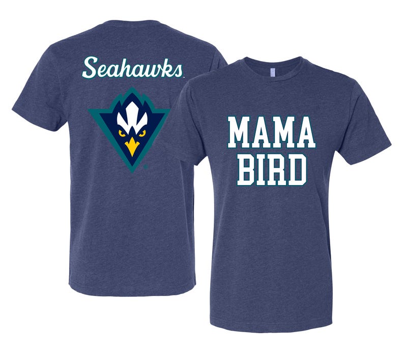 May include: Two navy blue t-shirts. One features the text "MAMA BIRD" in white block letters. The other shirt has the word "Seahawks" in white script on the back, above a teal, white, and yellow logo.