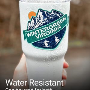 a person holding a white cup with a green virginia sticker on it