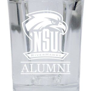 May include: A clear glass shot glass with a white design. The design features a stylized eagle with the text "NSU Riverhawks Alumni".