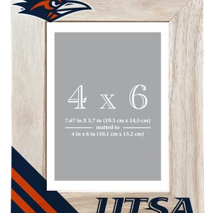 May include: A wooden picture frame with the text "4 x 6" and "UTSA". The frame is light-colored with a Roadrunner logo in the upper left corner. The frame dimensions are 7.67 in x 5.7 in (19.5 cm x 14.5 cm), matted to 4 in x 6 in (10.1 cm x 15.2 cm).