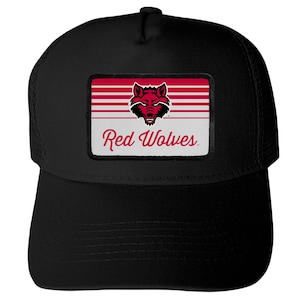 May include: A black trucker hat featuring a rectangular patch on the front. The patch displays a red and black wolf head graphic above the text Red Wolves in a red script font, set against a background of horizontal red and white stripes.