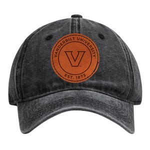 May include: A black, distressed baseball cap featuring a brown leather patch with the words "Vanderbilt University" and the letter "V" inside a circle. The text "EST. 1873" is also visible on the patch.