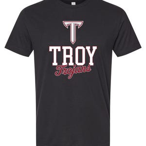 May include: A black short-sleeve t-shirt featuring a graphic on the chest. The graphic displays a large letter T in silver and maroon, the word TROY in white block letters with a maroon outline, and the word Trojans in maroon script font below.