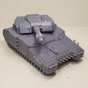 May include: A gray model tank with a detailed design. The tank features a central turret with a gun barrel, tracks, and various structural elements. The model is made of a solid, matte material.