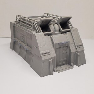May include: A grey model of a futuristic building with a door, vents, and a rooftop railing. The model has detailed paneling and a textured surface, suggesting a sci-fi or industrial theme.