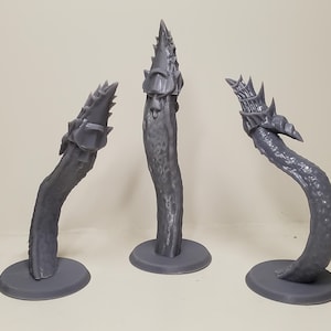May include: Three grey, unpainted 3D printed miniature figures, each featuring a long, textured, tentacle-like stalk rising from a circular base. The top of each stalk is adorned with a detailed, armoured, spiked, and segmented head-like structure.
