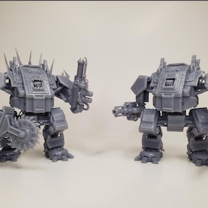 May include: Two grey, 3D-printed robot figures. One robot has a circular saw and a gun, the other has two guns. Both robots have a boxy torso, spiky details, and are standing upright.