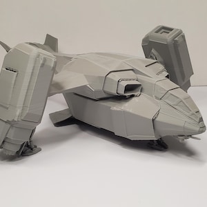 Op de afbeelding: Een grijs, 3D-geprint model van een futuristisch vliegtuig. Het model heeft een gedetailleerde cockpit, schuine vleugels en grote, rechthoekige motorbehuizingen. Het vliegtuig is ontworpen met scherpe hoeken en een getextureerd oppervlak.