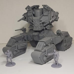 May include: A gray 3D-printed sci-fi tank model featuring a large central turret with mounted cannons and four tracked propulsion units. Two small humanoid soldier figurines stand in the foreground, providing a sense of scale to the vehicle.