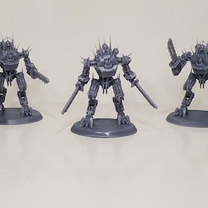 May include: Three grey robot figurines with spiked details and weapon attachments. Each robot stands on a circular base, showcasing a detailed mechanical design. The robots are posed in different stances.