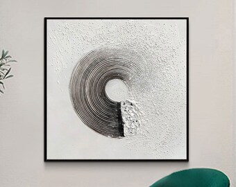 May include: A black and white abstract painting with a circular design hangs on a white wall above a green velvet armchair.