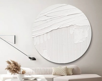 May include: A white circular abstract painting with textured brushstrokes. The painting is hanging on a white wall above a white couch with a throw pillow.